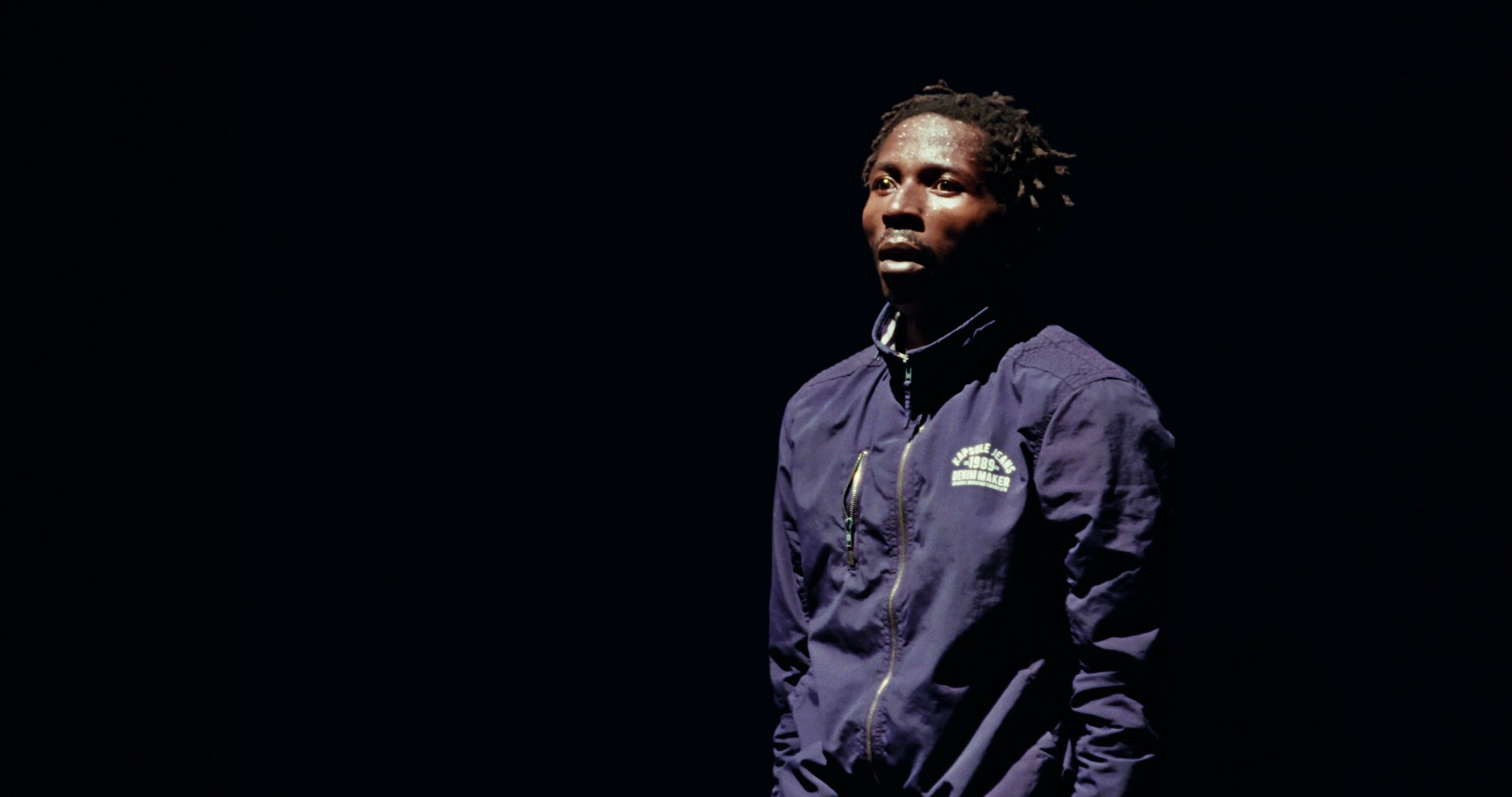 Léonce Noah, portrait en veste navy, clair-obscur, plan poitrine. Dézolé du Xilence.